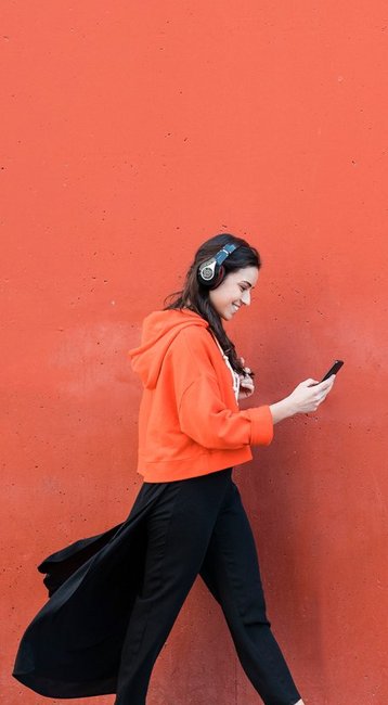 Studentin mit Handy in der Hand läuft an einer roten Wand vorbei